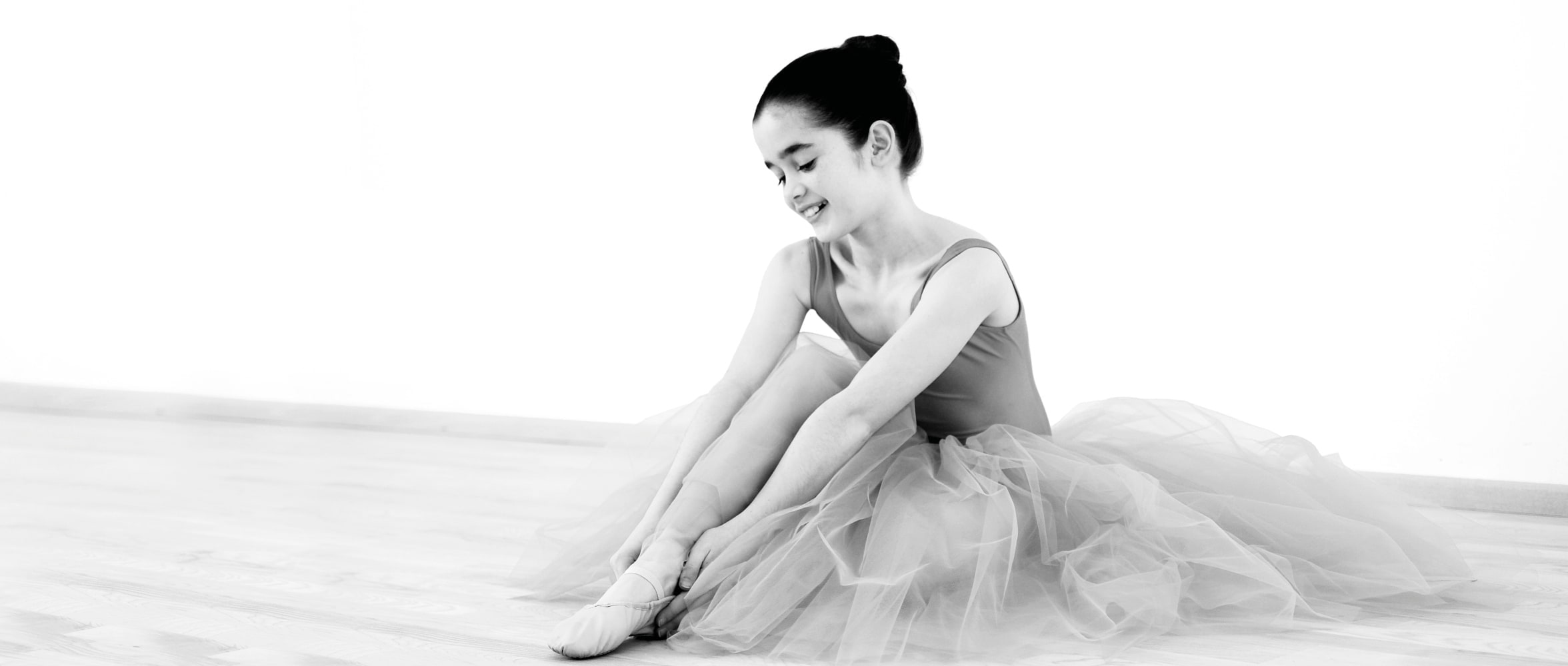 Junge Ballerina im Tüllrock sitzt auf dem Boden – Anmut & Ruhe im Kinderballett bei Nett & Friends Köln.