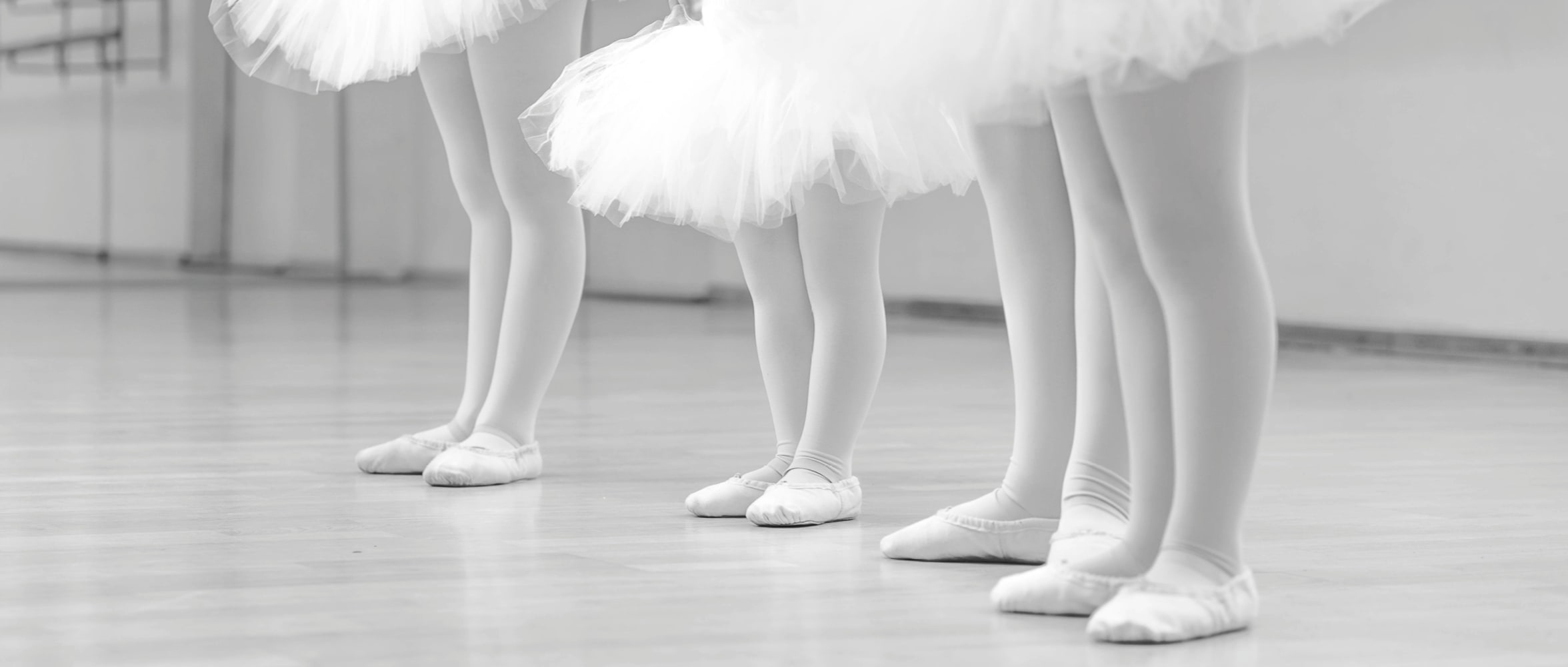 Kinderballett – Füße in Ballettschläppchen und weissen Tüllröcken beim Training