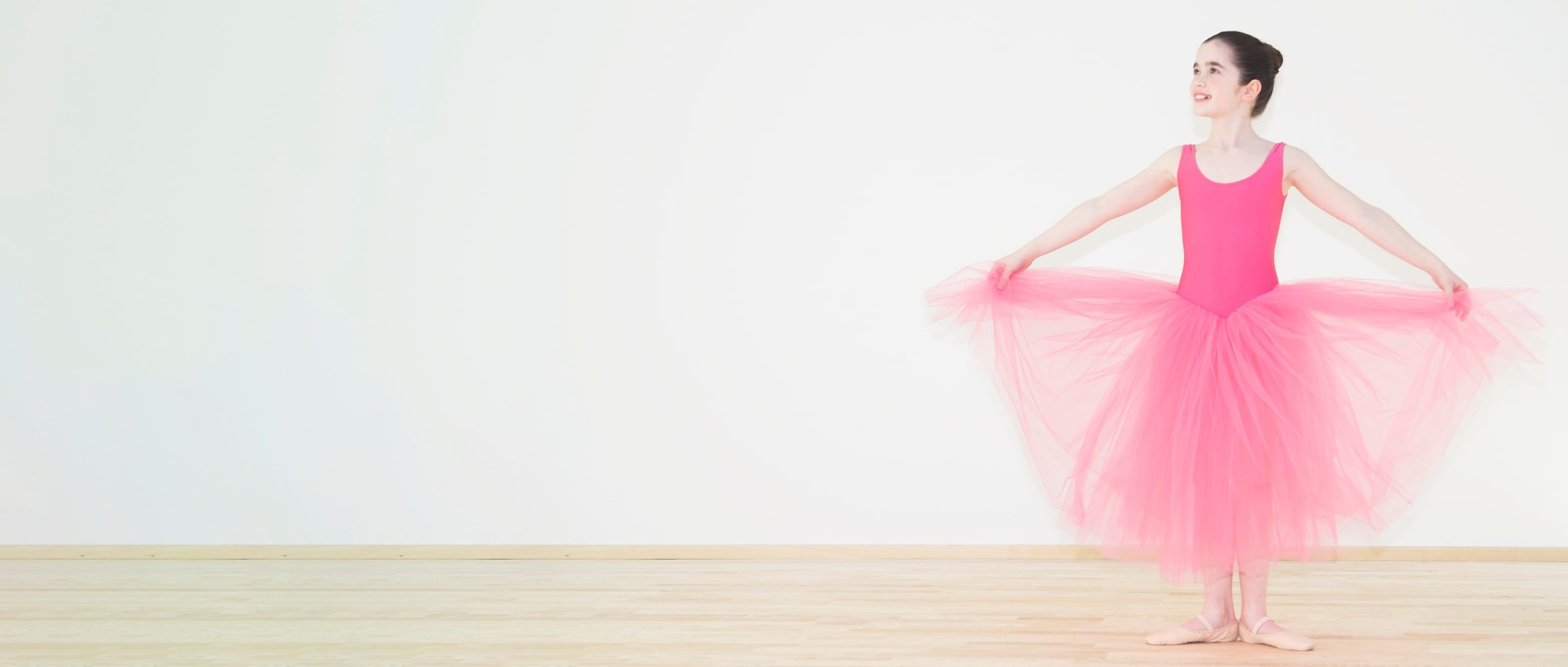 Ballerina im rosa Tüllrock hält den Rock elegant in einer klassischen Pose