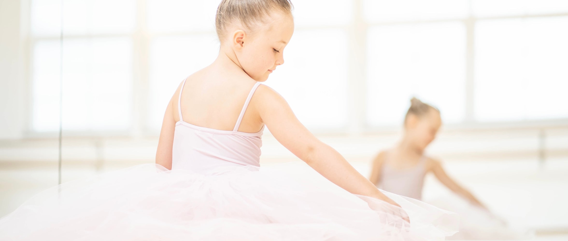 Ballerina im Tüllrock sitzt auf dem Boden vor dem Spiegel, von hinten fotografiert